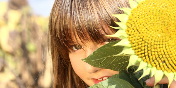 A young girl smiling while holding a vibrant sunflower, radiating joy and warmth.