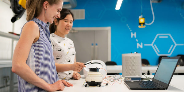 Two women collaborating in a lab, focused on a laptop, conducting research and analyzing data.