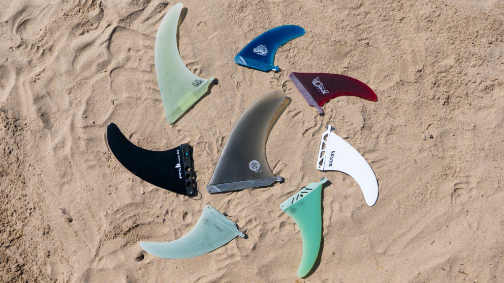Roundup of the 8 longboard single fins displayed in a circular pattern in the sand.