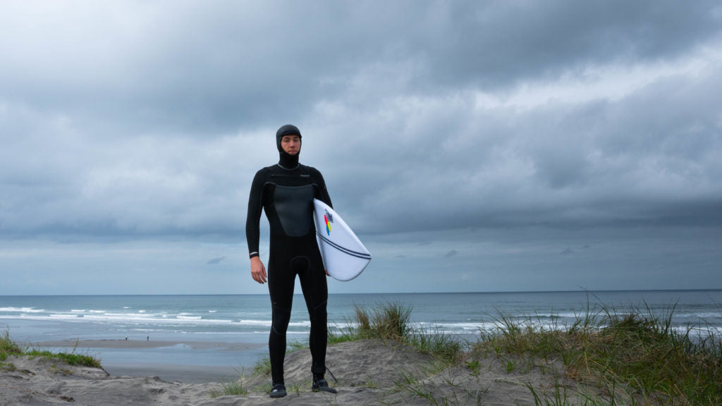 A surfer fully suited in the Marathon Sessions wetsuit holding their surfboard.