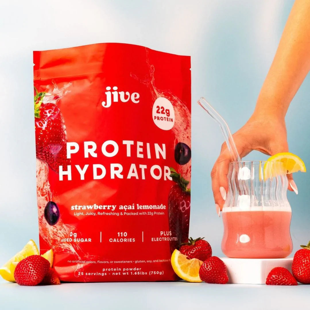 Red Jive Protein Hydrator pouch with a glass of strawberry acai lemonade, surrounded by strawberries and lemon slices.