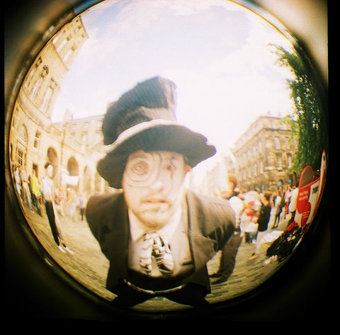 Fish-eye photo of Mad Hatter. White make-up with black circles and a black and white wonky top hat.