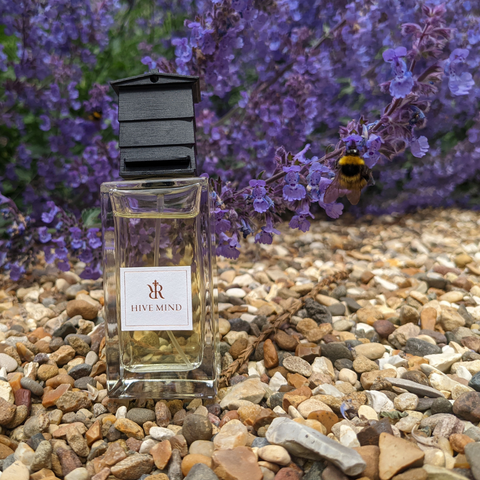 Hive Mind niche perfume next to a bee with flowers in the background