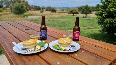 A table with two hot pulled pork and cider pies, two bottles of cider and views across Orange's wine country.