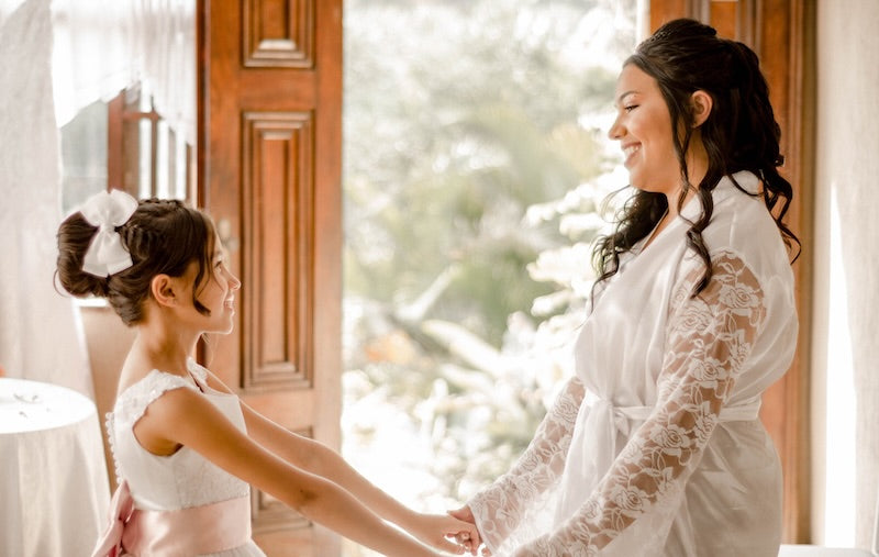 Woman and girl wearing white holding hands and smiling at each other.