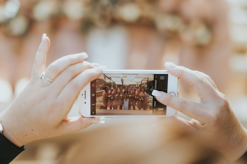 Person holding their phone up to video a bridal party.