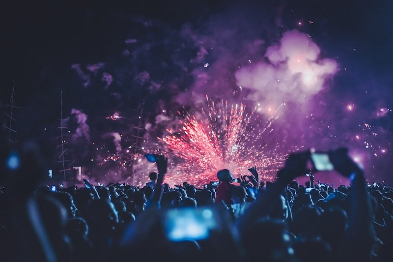 Fireworks go off behind an event with a crowd of people at night.