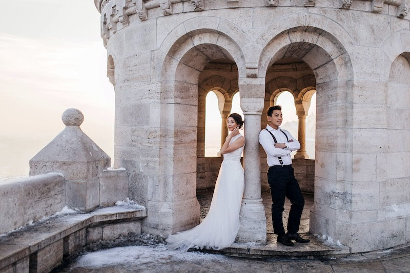 Wedding couple leaning against castle walls with snow on the ground.