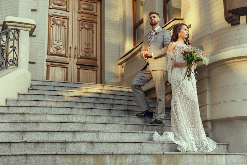 Bride and groom standing on steps of a ornate building.