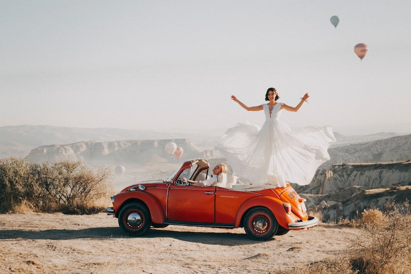 wedding couple in a red beetle car, with hot air balloons in the background.