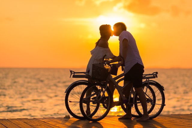 couple kissing in silhouette with while to bicycles by the ocean