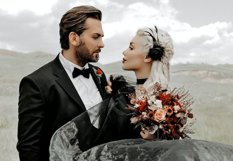 Man and woman stare into each others eyes. The man is wearing a black tuxedo and the woman a black wedding dress.