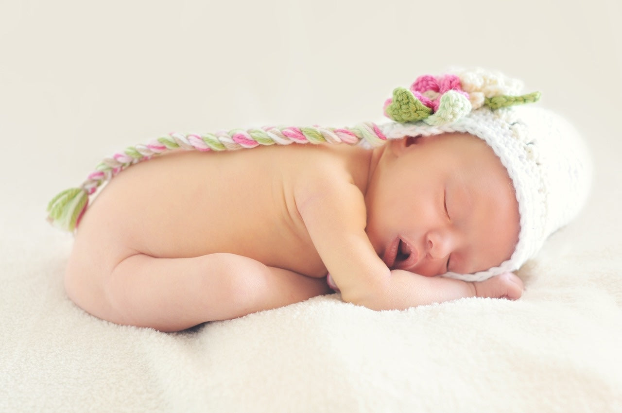 A newborn baby sleeps in a curled up position looking content.