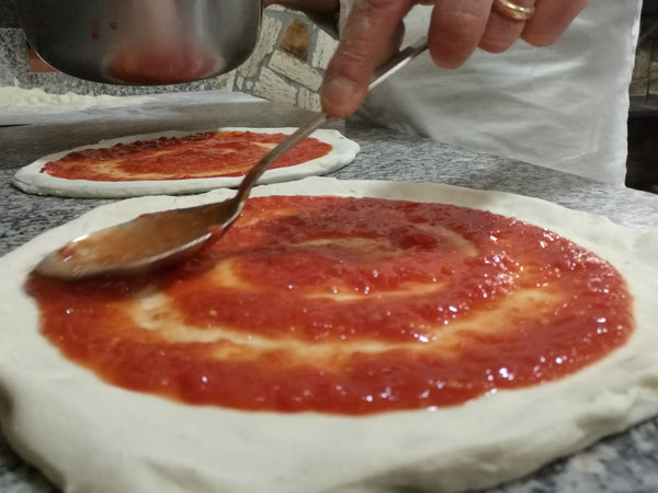 Ciao tomatoes being spread on pizza