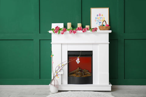Basket with Easter eggs, candles and tulips on fireplace near green color wall.
