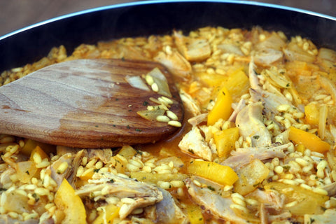 Closeup of chicken and pepper paella in a pan with wooden spoon