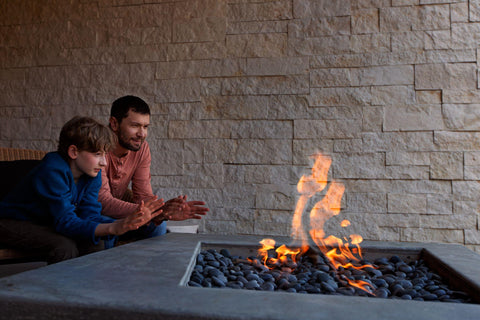Father and son warming up by gas fire pit.