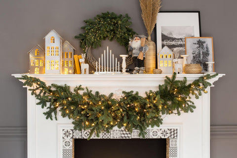 Fireplace with christmas decorations standing on it and fir branches and garlands hanging on it