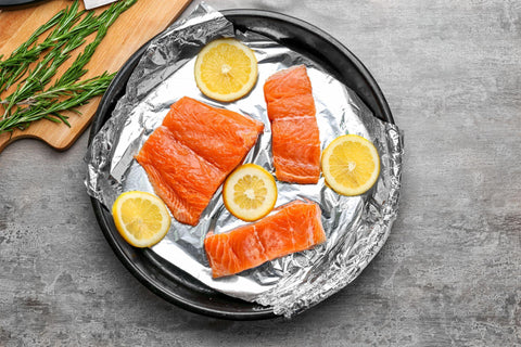 Frying pan with foil, slices of lemon and salmon on light table