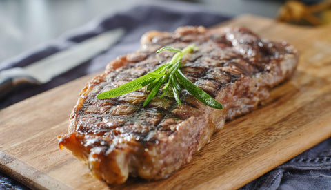 grilled new york strip steak resting on wooden cutting board