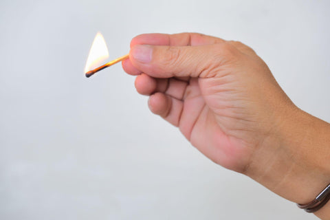 Hand holding a burning matchstick over white background.