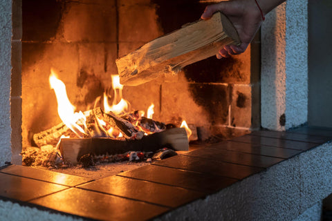 Hands putting firewood in a kindled fireplace.