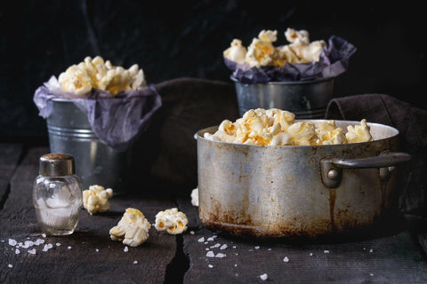 Prepared salted popcorn served with sea salt in small buckets and vintage aluminum pan on old wooden kitchen table.