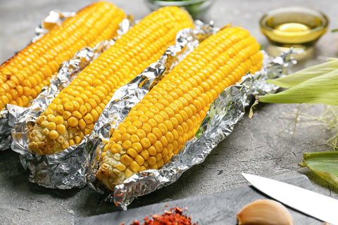 Tasty baked corn cobs on grey background