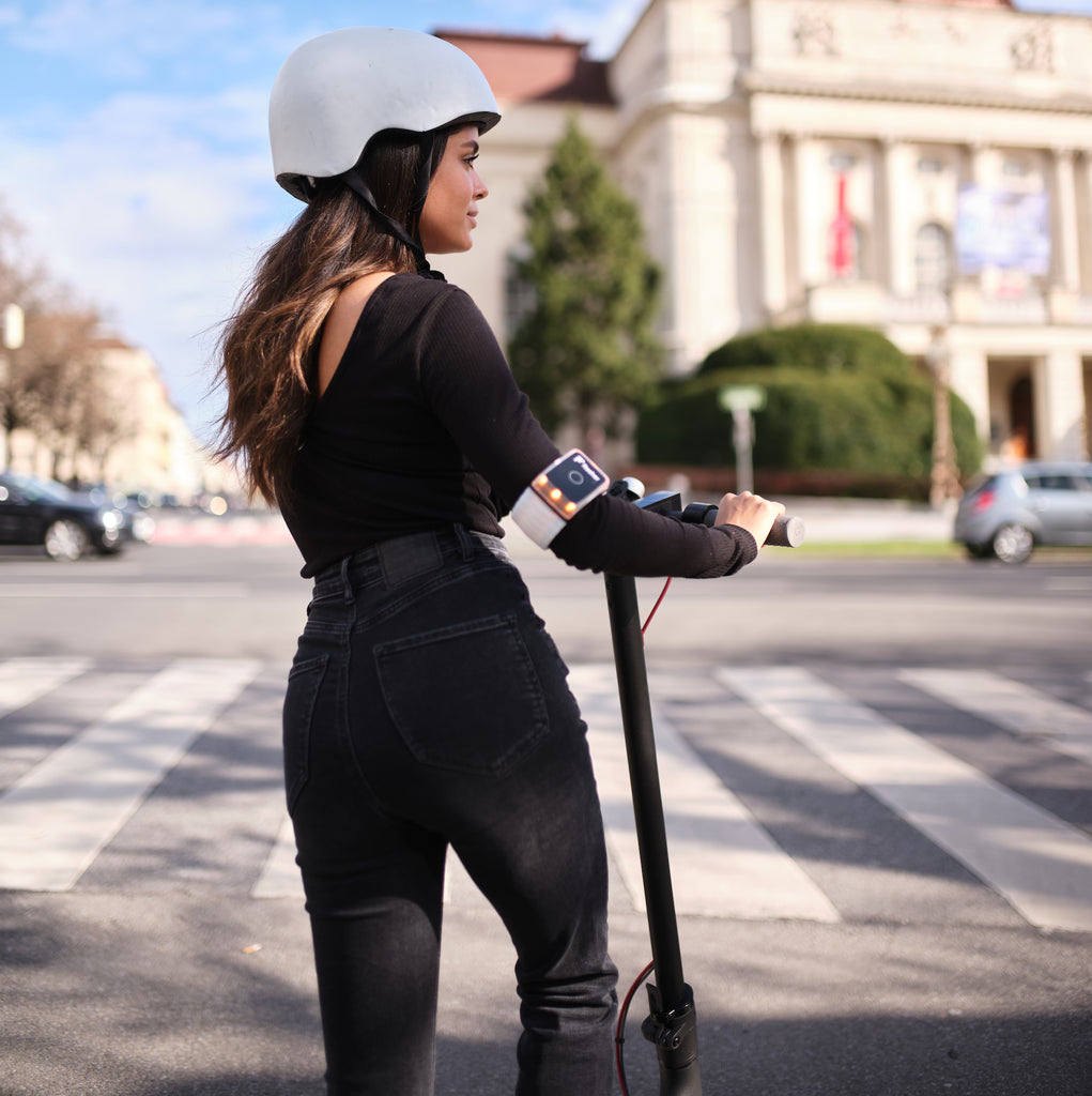 Junge Dame mit weißem Helm steht auf E-Scooter an der Kreuzung. Heller Tag.
