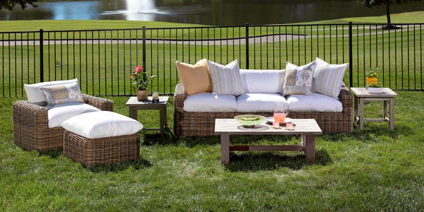 Azza Outdoor collection image featuring a wicker sofa, a wicker lounge chair, and a wooden table in a sunny backyard.