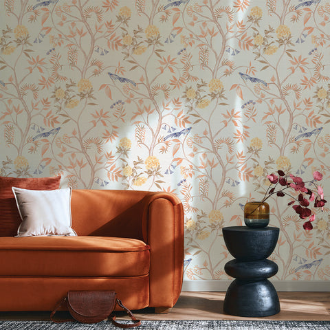 Printed chinoiserie grasscloth wallpaper is applied to a wall behind an orange couch.