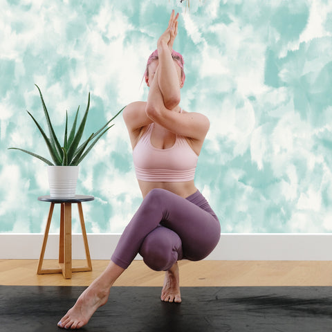 Woman doing a yoga pose in front of aqua blue peel and stick wallpaper by Tempaper.