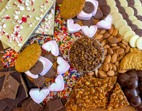 Chocolate, peppermint bark, nuts, sprinkles, marshmallows, chocolate buttons on a food board