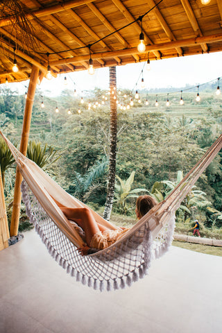 Women laying on  macrame hammock over looking palm trees