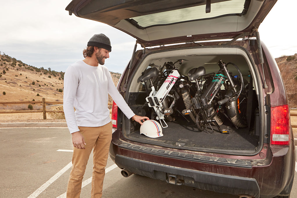 GOTRAX White and Black EBE4 Off-Road Fat Tire Electric Bikes for Adults with Front Wheel Suspension in the Folded Position in the trunk of a car