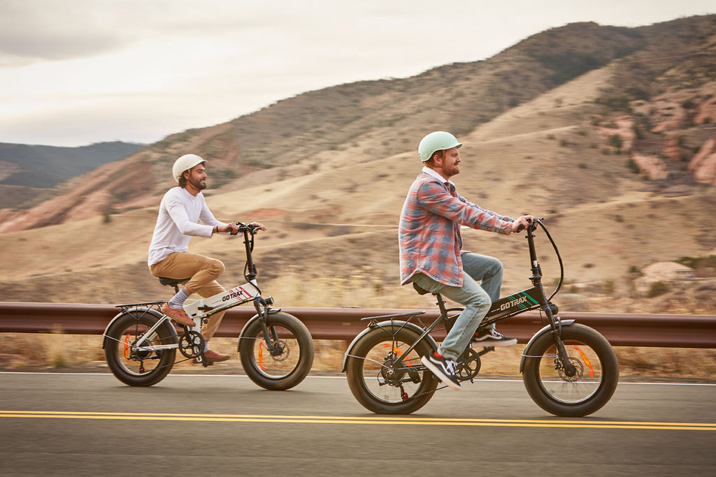 Two people riding GOTRAX White and Black EBE4 Off-Road Fat Tire Electric Bikes for Adults with Front Wheel Suspension