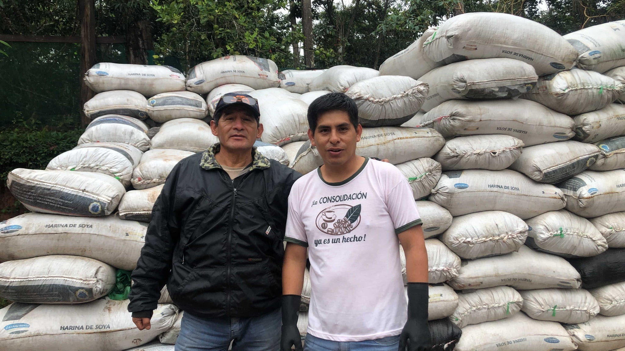 Picutre of 2 farmers from chacra d'dago biodynamic farm in villa rica peru behind a lot of packed green coffee