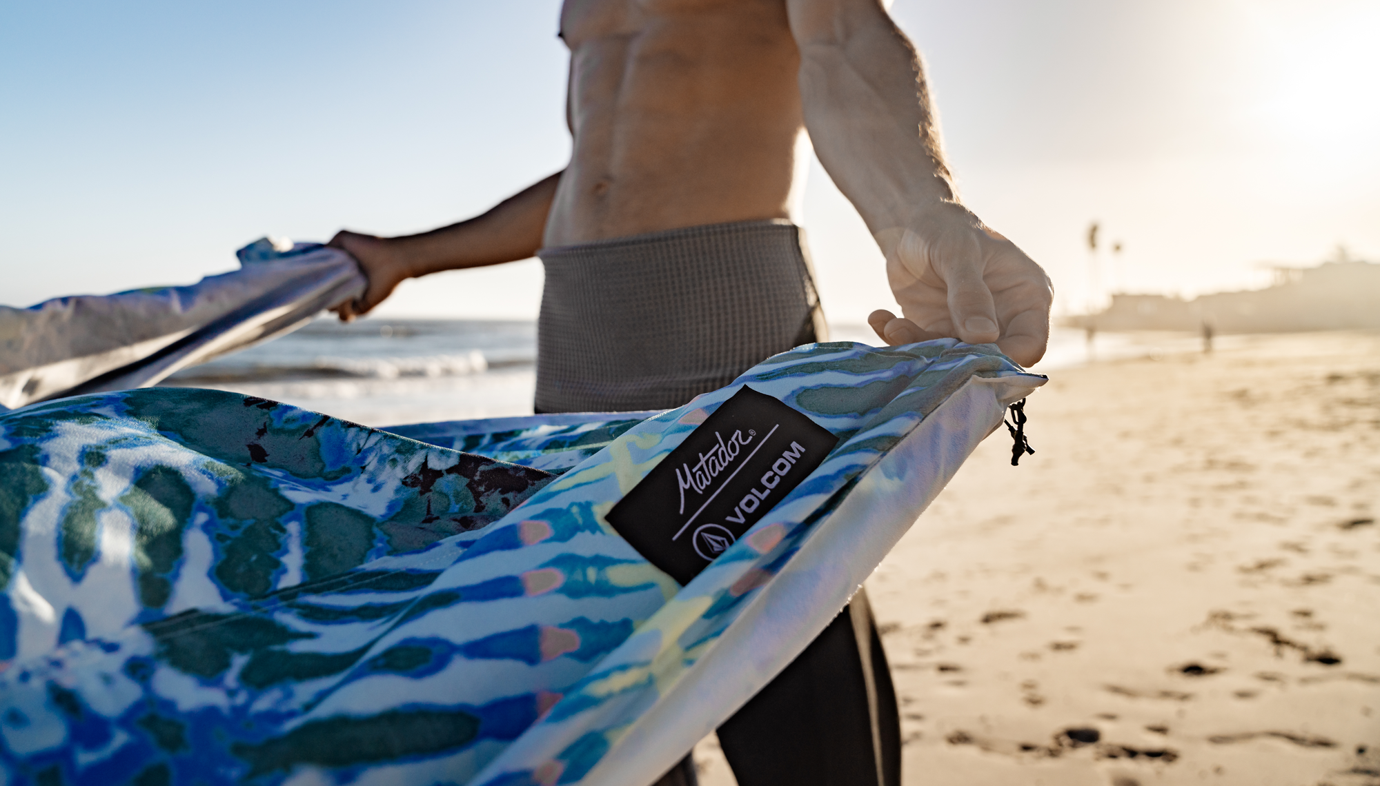 Man on beach, unfurling Tie Dye towel