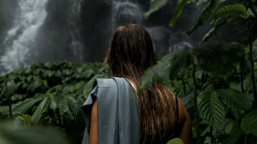 Woman with towel over her shoulder, standing in lush waterfall forest