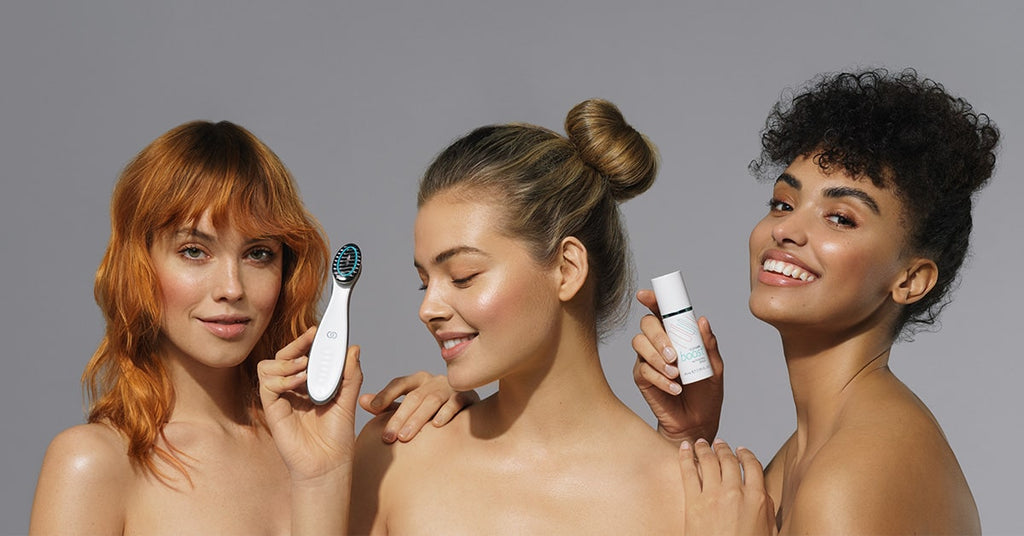 Drei junge Frauen mit glatter strahlender Haut halten lächelnd die ageLOC boost Produkte in den Händen. Sie sind bis zu den Schultern zu sehen.
