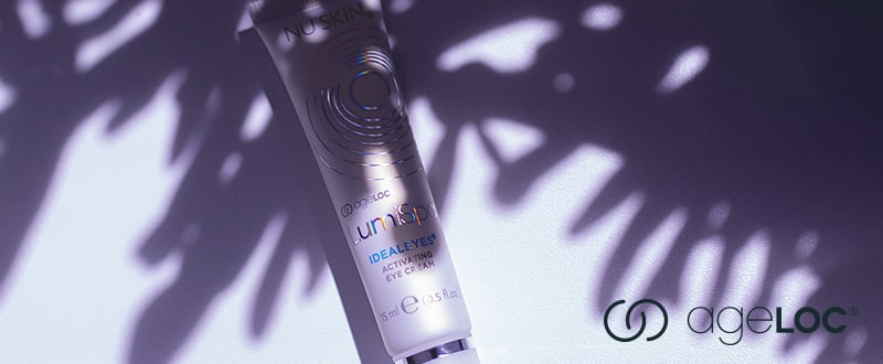 Nu Skin IdealEyes ergänzendes Gel zum LumiSpa (15ml) liegt auf weißer Oberfläche, das Schattenspiel einer Pflanze hebt reflektierende Elemente der Tube hervor.