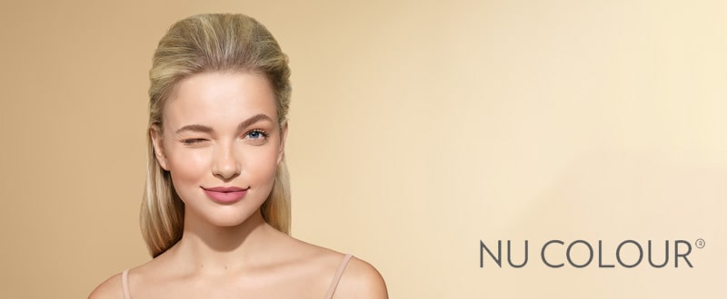 Junge Frau mit blonden Haaren trägt auf bemalten Lippen ein verspieltes Lächeln. Das Bild wurde mit dem Nu Colour Logo von NuSkin in der rechten unteren Ecke gebrandet.