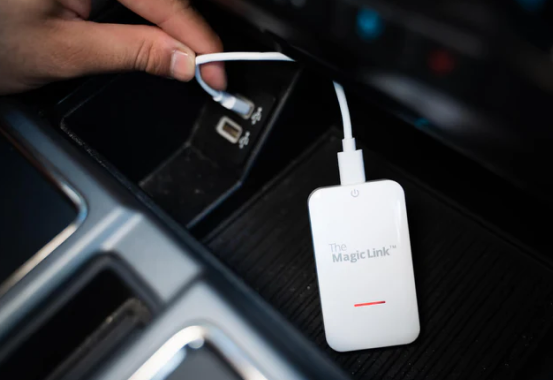 A hand connecting a cable to a device labeled 'The Magic Link' in a car interior.