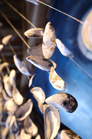 Sculpture faite tout en suspension de moules bleues vue de dessous avec un fond bleu ou tourbillone des halots de lumière