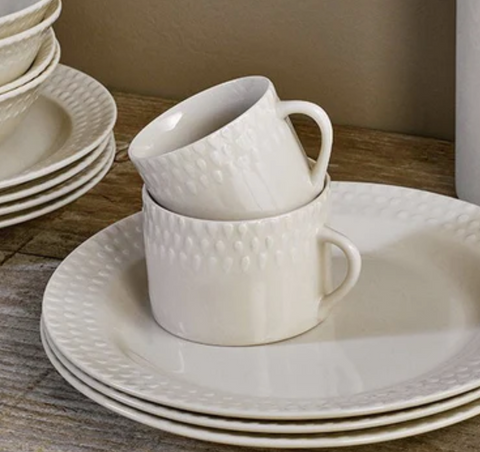 A product image of two cream mugs stacked on top of eachother. The cups are stood on a stack of plates in the same colour.