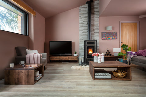 An image of a cozy living room with a wooden coffee table in the center, a fireplace, and a comfortable couch. The living room has a modern design with a wooden floor and a large rug. There is also a window and a door.