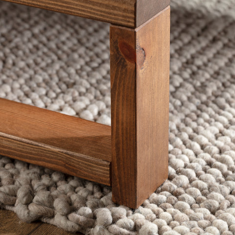 A close up of a wooden coffee table on a light cream bobbled rug.