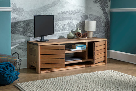 An image of a living room with a wooden TV stand. On the TV stand there is a TV, lamp and some decorative items. The wall behind the TV stand has a wallpaper with a forest design.