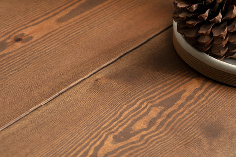 A close-up of a wooden coffee table. In the top right corner is part of a ceramic dish with pine cones inside.