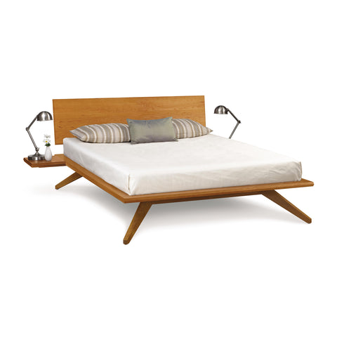 A modern-contemporary Astrid Cherry Platform Bed by Copeland Furniture with a white mattress, striped and solid pillows, and two bedside tables with lamps.